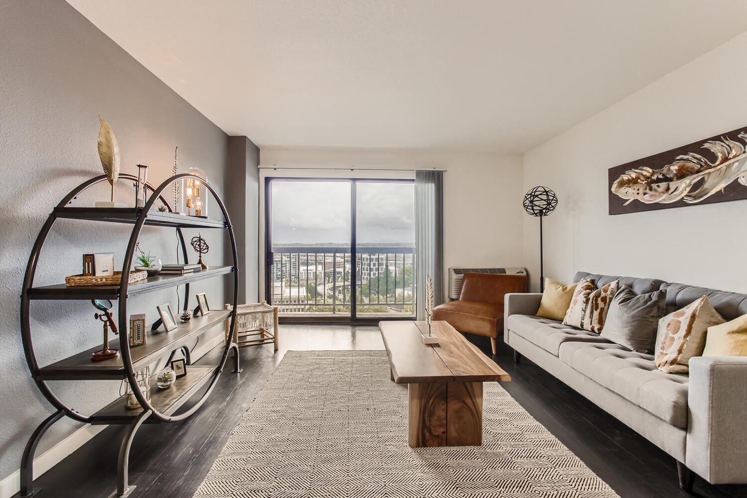 Modern Apartments in Downtown Portland, OR - Linc 301 - Living Room with Plank Flooring, Sofa, Leather Chair, Wooden Coffee Table, and Sliding Glass Door to Europea-Style Balcony.